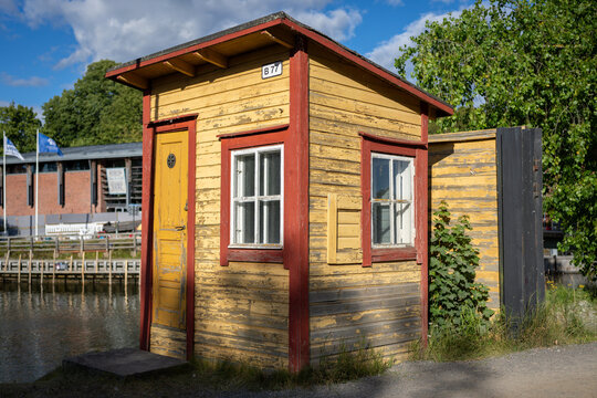 Weathered yellow wooden hut beside the water in a leafy Helsinki waterfront setting