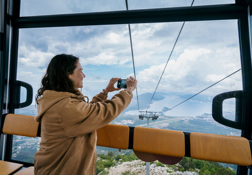 Young woman taking photo with smartphone from Kotor cable car cabin in Montenegro