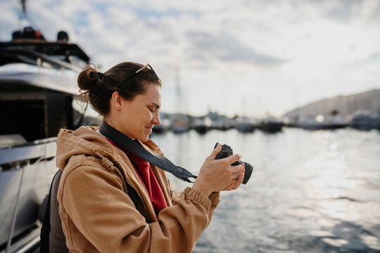 Young woman photographer holding camera in marina with luxury yachts background
