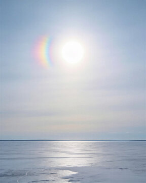 A clear vertical sun dog rainbow phenomenon reflecting brilliant spectral light over an endless expanse of frozen winter sea ice.