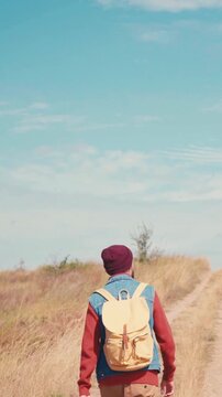 Hiker walking on country path wearing backpack under blue sky rear view