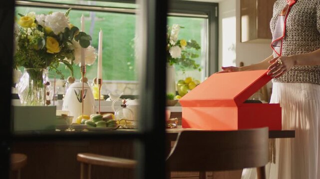 Woman opening red gift box at festive dining table with flowers
