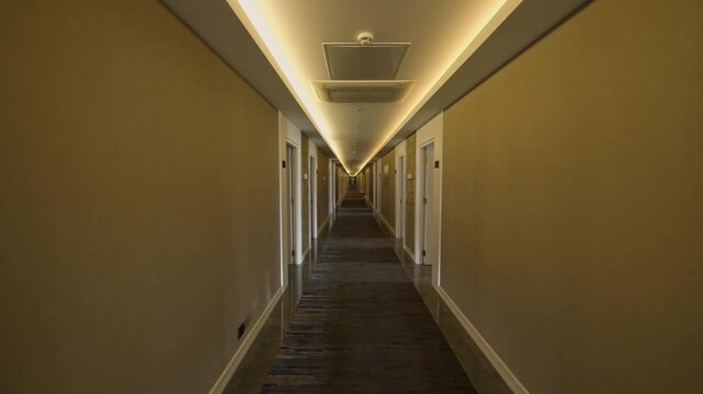 A modern hotel corridor features guest room doors on both sides, patterned carpeting and warm recessed ceiling lights. This symmetrical hallway leads toward the far end of a quiet accommodation floor.