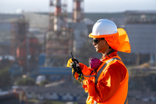 Industrial worker in orange protective clothing coordinating by radio at an industrial plant