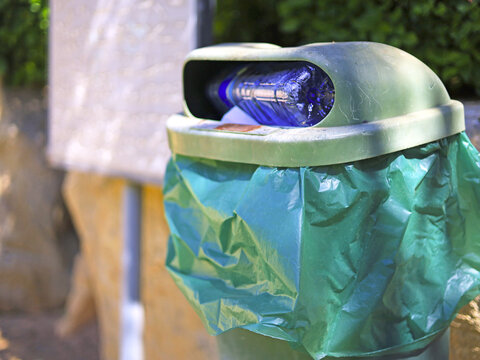 Plastic bottle rests in the opening of a lined outdoor bin, with disposable packaging discarded in a public sanitation container at the point of waste collection and litter disposal in shared spaces.