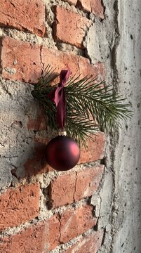 Burgundy Christmas ornament with velvet ribbon and pine sprig hanging on exposed brick wall