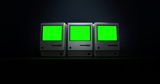 Three vintage personal computers turning on revealing blank green screens on concrete table in dark dramatic room