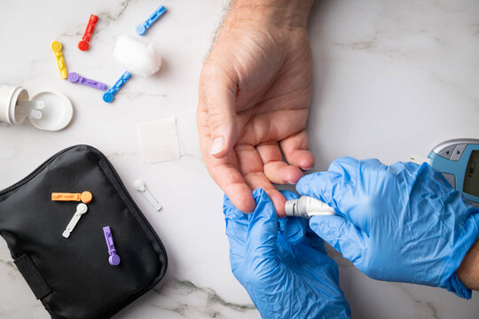 Healthcare professional wearing blue gloves prepares to obtain a blood sample for glucose monitoring of a patient via finger stick.