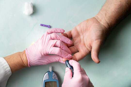 Healthcare professional wearing pink gloves prepares to obtain a blood sample for glucose monitoring of a patient via finger stick.