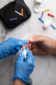 Healthcare professional wearing blue gloves prepares to obtain a blood sample for glucose monitoring of a patient via finger stick. Vertical