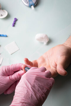 Healthcare professional wearing pink gloves prepares to obtain a blood sample for glucose monitoring of a patient via finger stick.