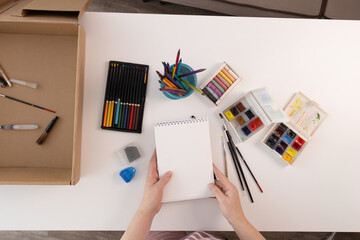 Woman arranges art supplies on a bright craft table for hands-on screenless creativity © olga_sova
