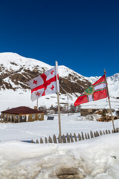 National flag with five red crosses and a second flag waving above a snowy village, Samegrelo-Zemo Svaneti, Ushguli, Georgia