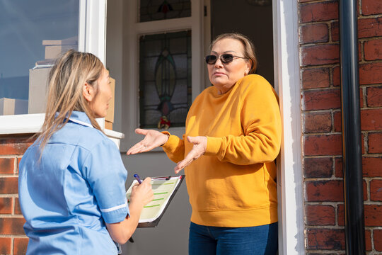 Nurse interviews patient at  front door of home and records information on clipboard. A home healthcare visit 
