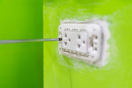 Close-up Hand of an electrician using a screwdriver to install a new electrical outlet in a concrete wall at home.