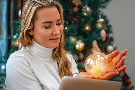 Woman examines a glowing ornament beside a Christmas tree