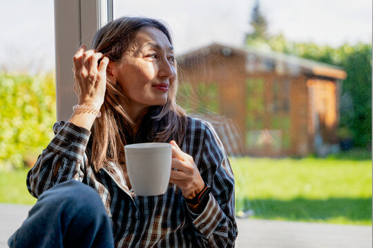 Woman holding a cup by a window in a home during daytime
