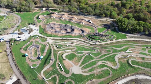Winding mountain bike paths snake across Region community sports grounds along Denton County. Terraced dirt berms border paved pedestrian access points, manicured field edges, Frisco, Texas