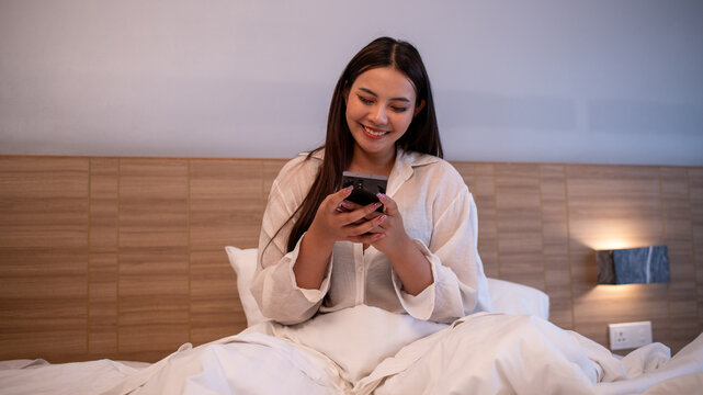Young woman on bed in cozy bedroom using smartphone and browsing online modern lifestyle digital communication and everyday leisure.	