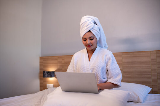 Young woman relaxing on bed while using a laptop and enjoying music or online content.	