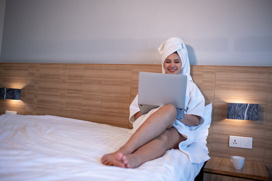 Young woman relaxing on bed while using a laptop and enjoying music or online content.	