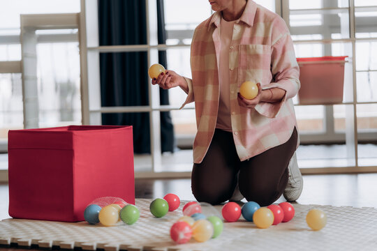 Close view of hands holding colorful play balls above soft rug beside open storage box illustrates tactile sorting and hands on home management practices with relatable detail with color sorting.
