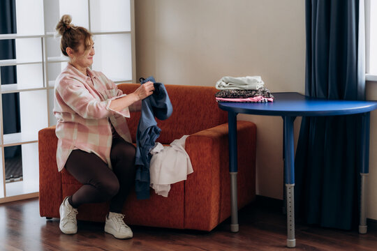 Woman kneeling beside orange armchair while sorting denim from clothing pile illustrates practical closet reset and clothing reuse in compact multifunctional urban home reflecting circular fashion.