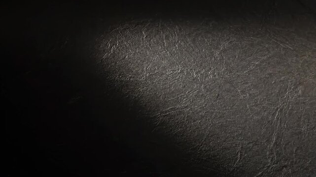 A light source from the upper left falls across a dark, textured surface, revealing fine ridges and irregular marks in a close-up