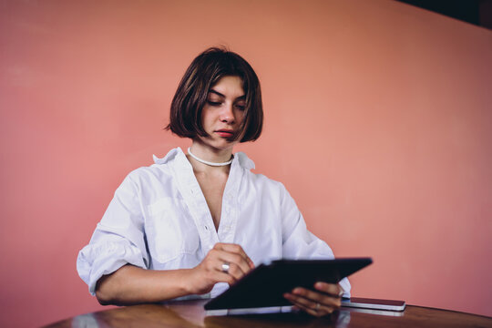 Cozy productivity smart tech integration lets focused Caucasian female freelancer use electronic stylus pen on tablet touchscreen device, maintaining flexible workflow during online study