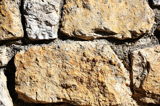 Large rough limestone blocks wall texture with deep shadows between sunlit weathered stones, natural beige masonry surface, old architecture background for construction, design and building materials