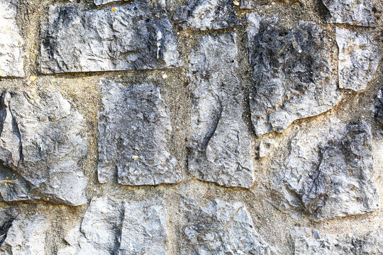 Rough gray limestone wall texture with irregular rocks set in sandy mortar, weathered masonry surface with lichen spots, old architecture background for construction