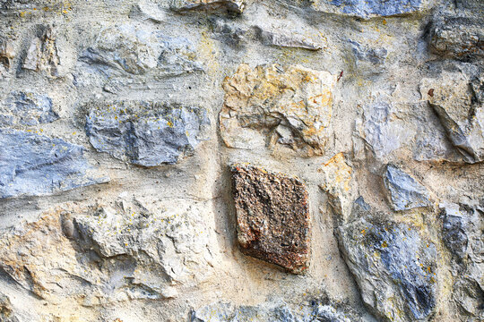 Rustic stone wall texture with colorful irregular rocks and lichen in thick cement mortar, weathered masonry surface with brown, gray and beige stones, old architecture background
