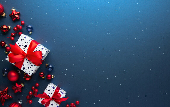 Blue Christmas and Happy New Year holiday background with gift boxes, red ribbon bows and festive red ornaments, flat lay with copy space. Greeting card.