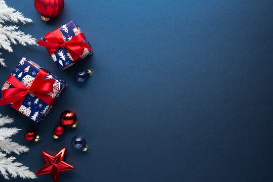Blue Christmas and Happy New Year holiday background with gift boxes, red ribbon bows and festive red ornaments, flat lay with copy space. Greeting card.