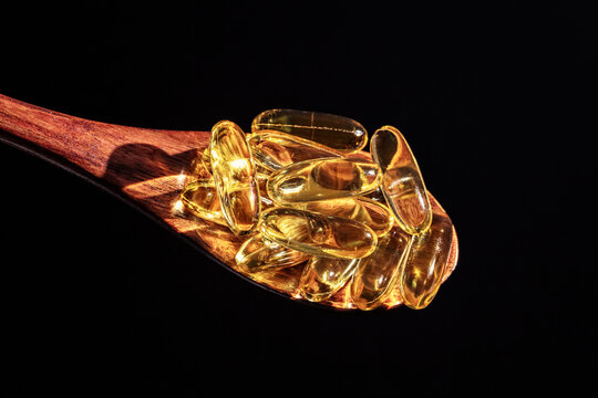 Fish oil capsules with Omega 3 or Vitamin D on a wooden spoon