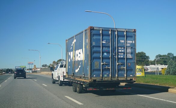 Wilmington, Delaware, U.S.A - Oct 18, 2026 - A pickup truck towing a flatbed trailer carrying a large blue CMA CGM shipping container.