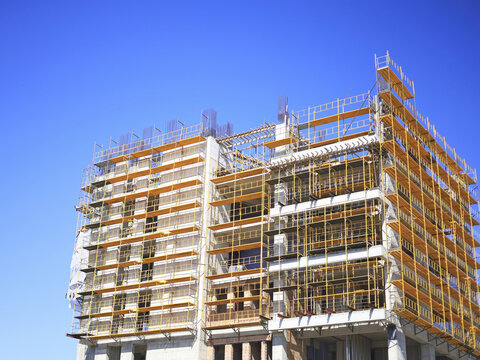 Unfinished concrete building wrapped in scaffolding beneath a clear sky shows a structural stage of real estate development, with exposed floors and masonry defining a multistory construction project.