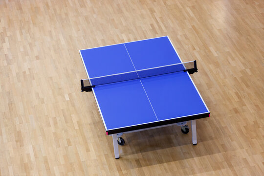 Blue Table Tennis Table with Net on Wooden Parquet Floor in Indoor Sports Hall. Equipment for Recreation, Fitness, Training, and Competitive Play