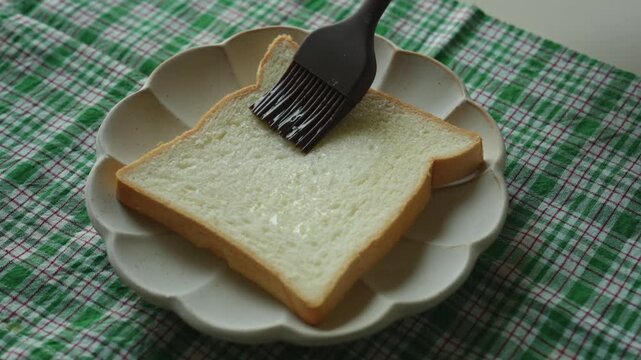Brushing a slice of white bread with a silicone brush on a plate