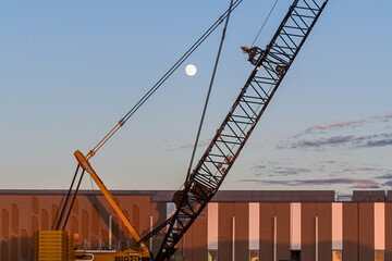 Large lattice boom crane at a data center construction site with the moon visible in the afternoon sky, illustrating heavy equipment, industrial development, and digital infrastructure expansion © Eduardo Barraza