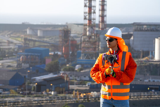 Industrial worker wearing safety gear and holding a respirator at a refinery