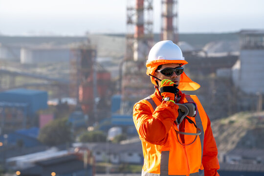 Industrial worker in high-visibility safety gear communicating by radio at a busy worksite