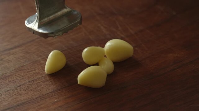 Crushing garlic cloves with a metal press on a wooden cutting board