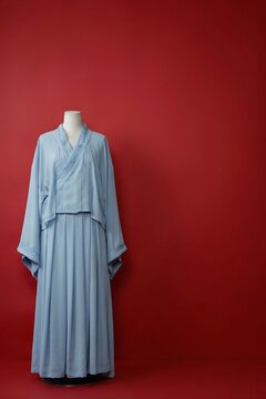 Traditional light blue hanfu dress displayed on a mannequin against a vibrant deep red background