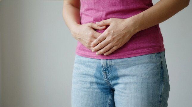 A close-up of a woman pressing her hands against her lower abdomen with a visible wet stain on her blue jeans, symbolizing urinary incontinence, bladder leak, or accidental wetting concepts.