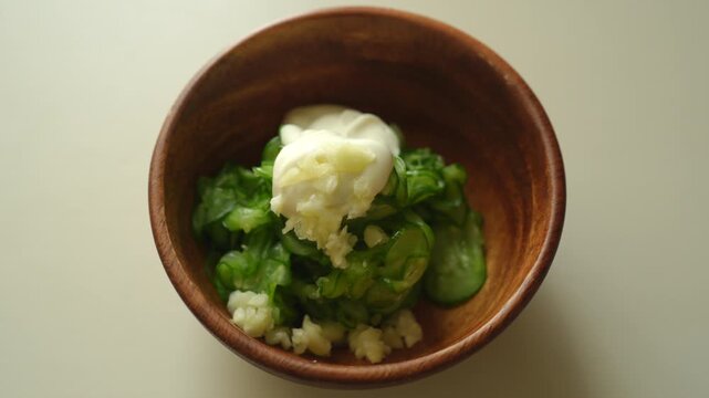 Sprinkling chopped garlic onto cucumber and mayonnaise in a wooden bowl