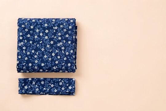 Folded stack of dark blue fabric with small white floral pattern on a light background