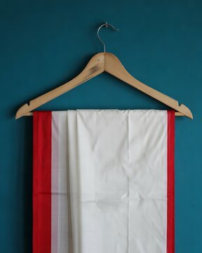 Traditional white and red indian saree hanging on a wooden clothes hanger against blue wall