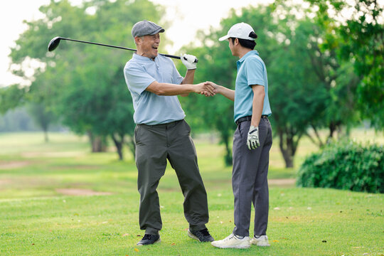 Active aging and golf friendship concept. Happy senior golfer shakes hands with a younger man on a green golf course, celebrating a friendly game. Golf, senior, handshake, friendship, sports.