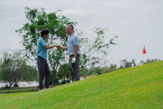Active aging and golf friendship concept. Happy senior golfer shakes hands with a younger man on a green golf course, celebrating a friendly game. Golf, senior, handshake, friendship, sports.